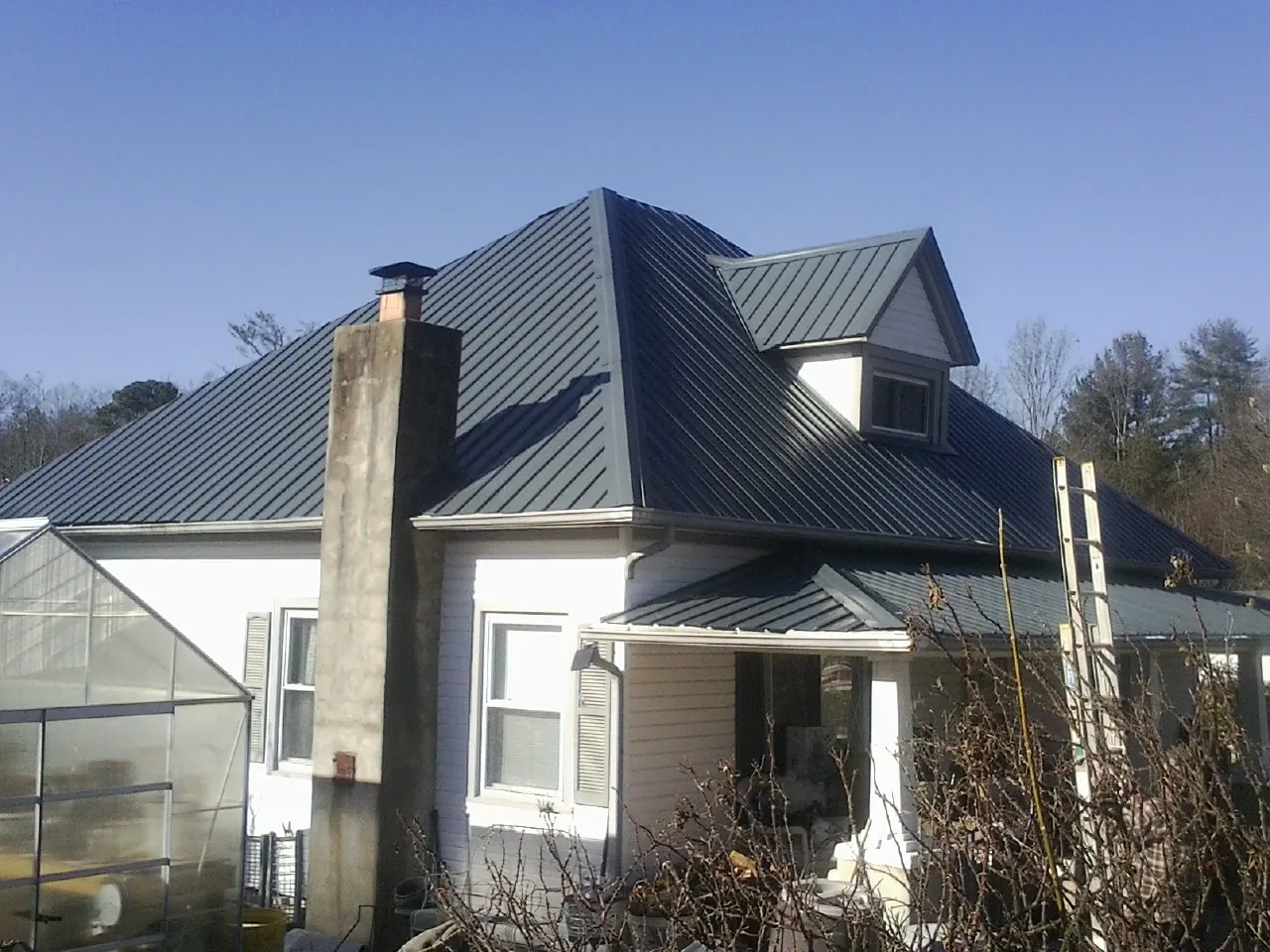 Dark blue standing seam metal roof on a white farmhouse with dormer — Slate & Tile Roof Repair by Roofing Brothers in New Boston