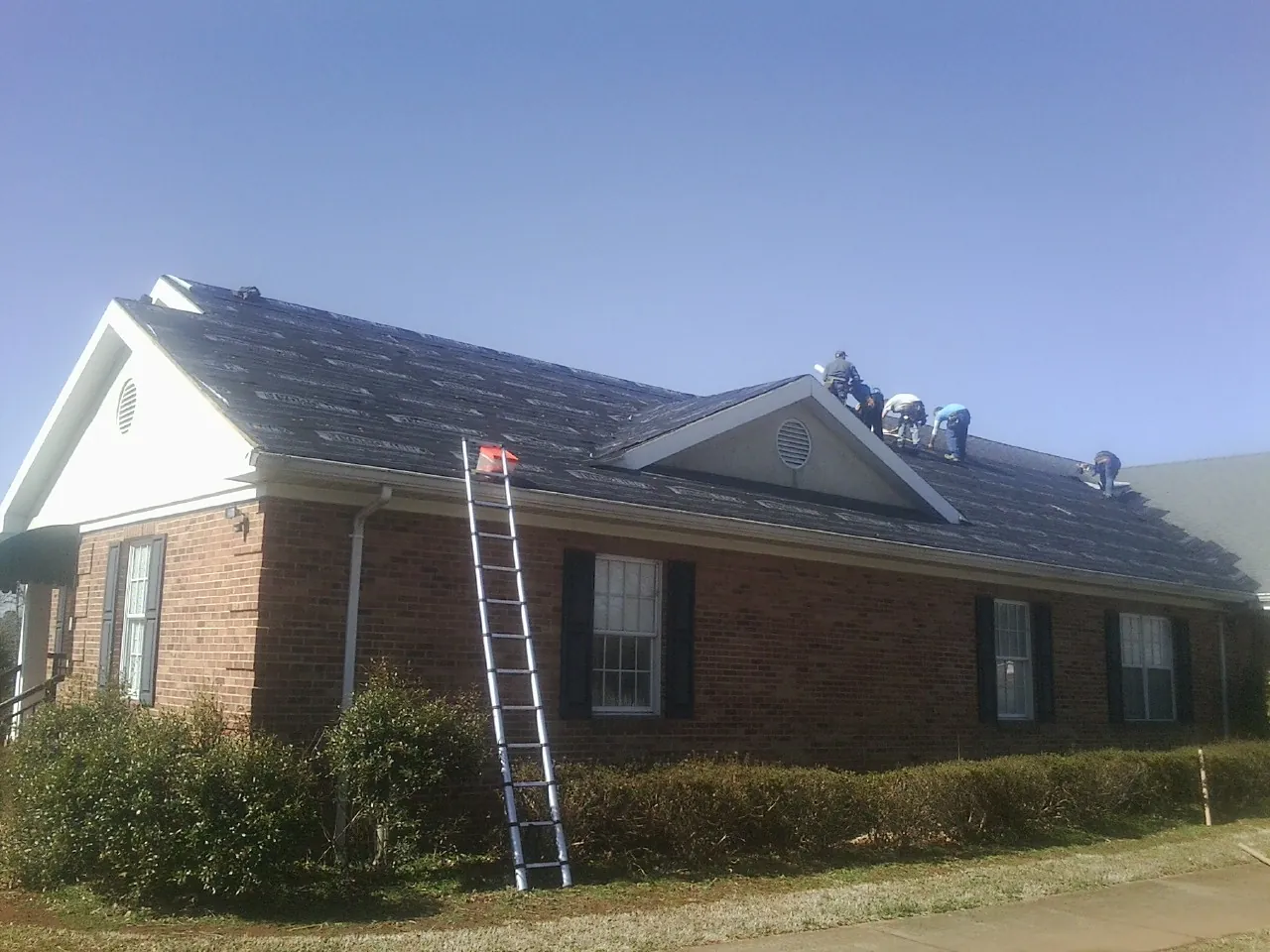 Crew tearing shingles off a brick ranch roof with a ladder set — Emergency Roof Repair work by our crew in New Boston