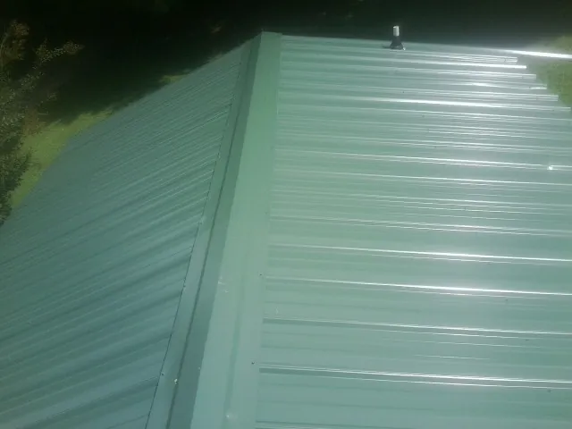 New green metal panels meeting at the ridge of a roof — Flat Roof Repair work by our crew in New Boston