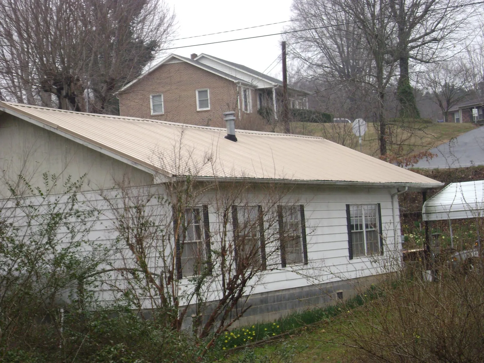 Tan metal roof on a white sided house set into a hillside — Commercial Roofing by Roofing Brothers in New Boston