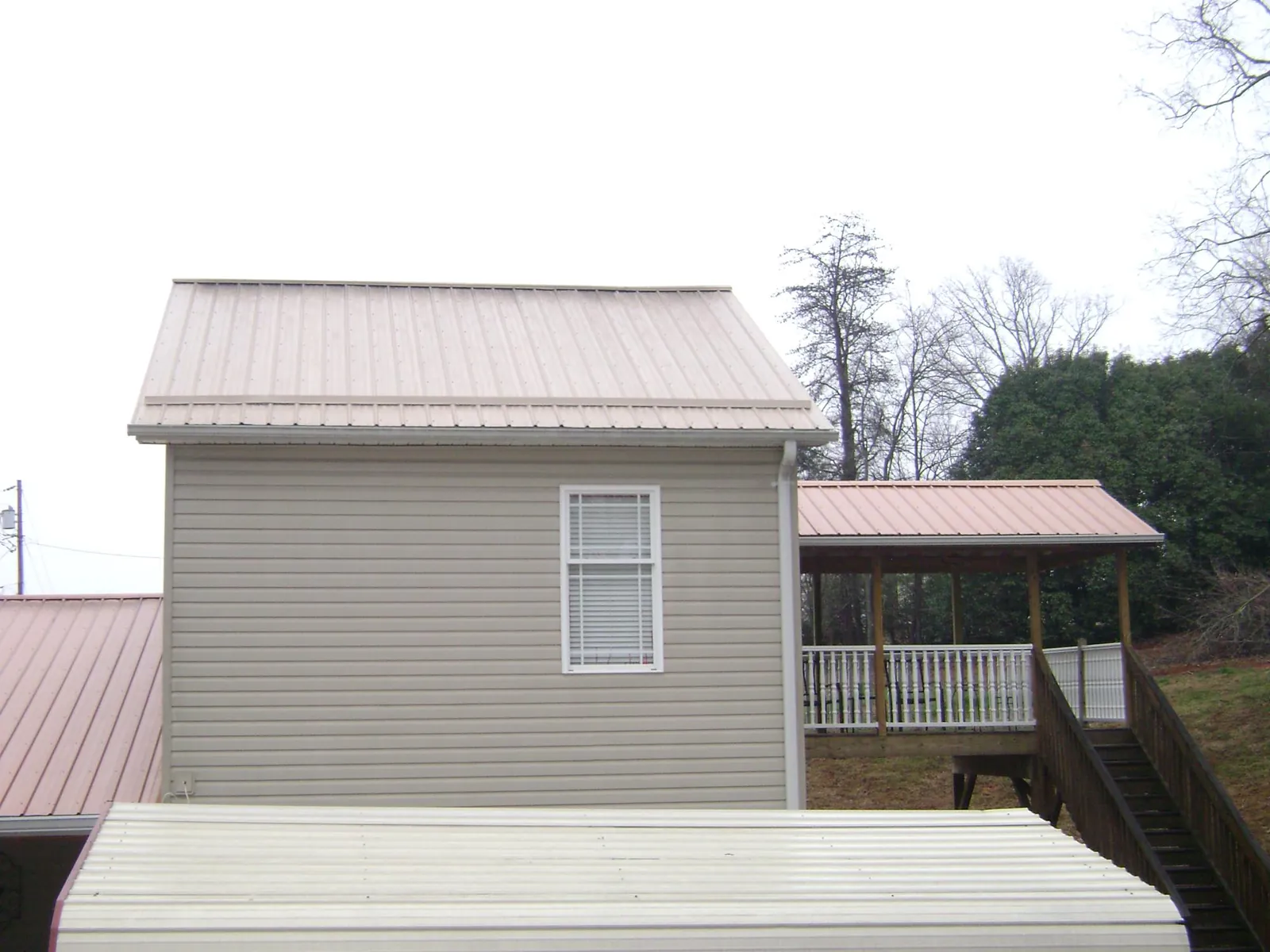 Tan metal roofs on a two story addition and attached porch, from a Roof Replacement job in New Boston
